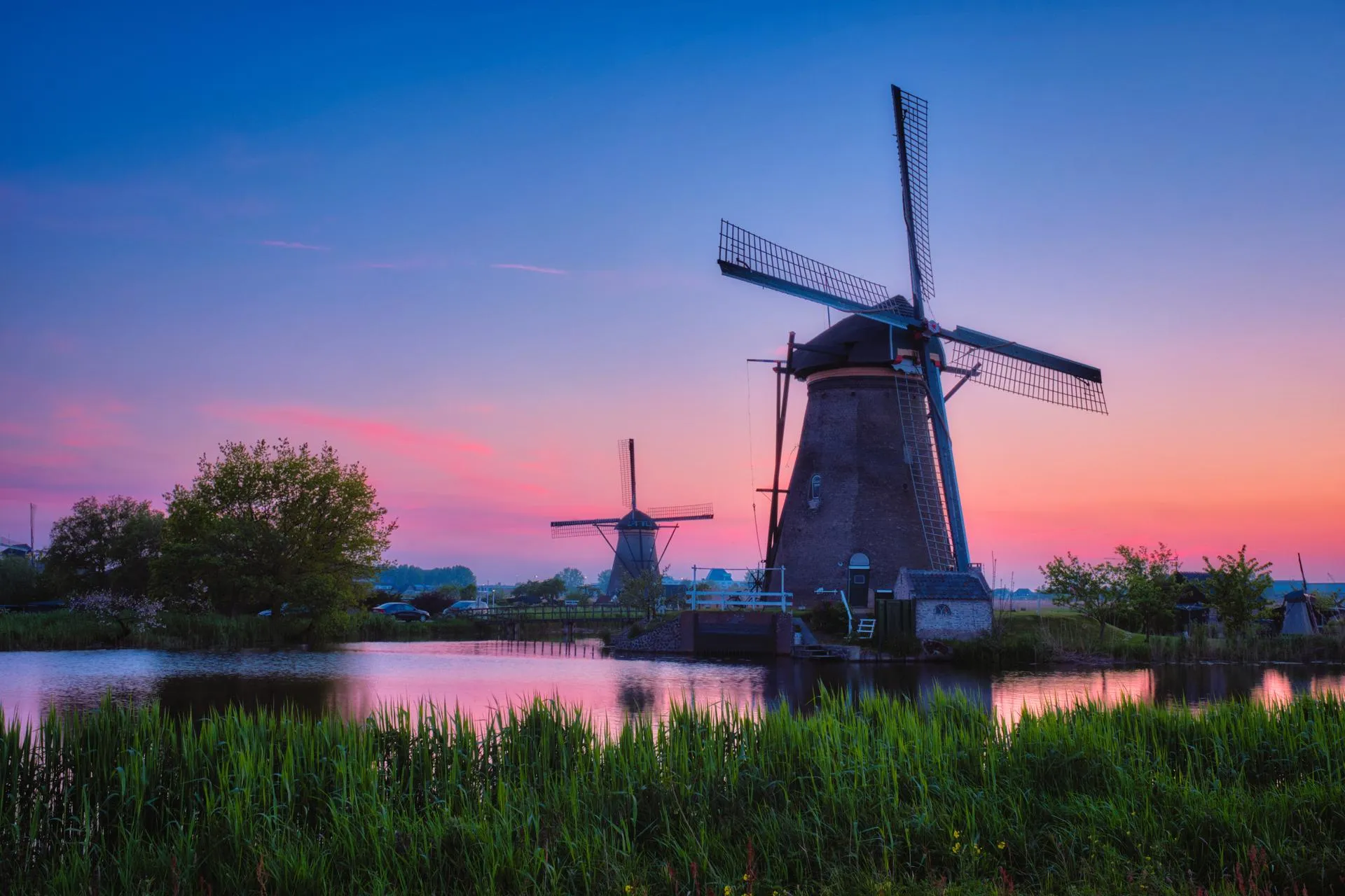 Windmills at Kinderdijk at dusk, reflected in the water behind a bank of reeds