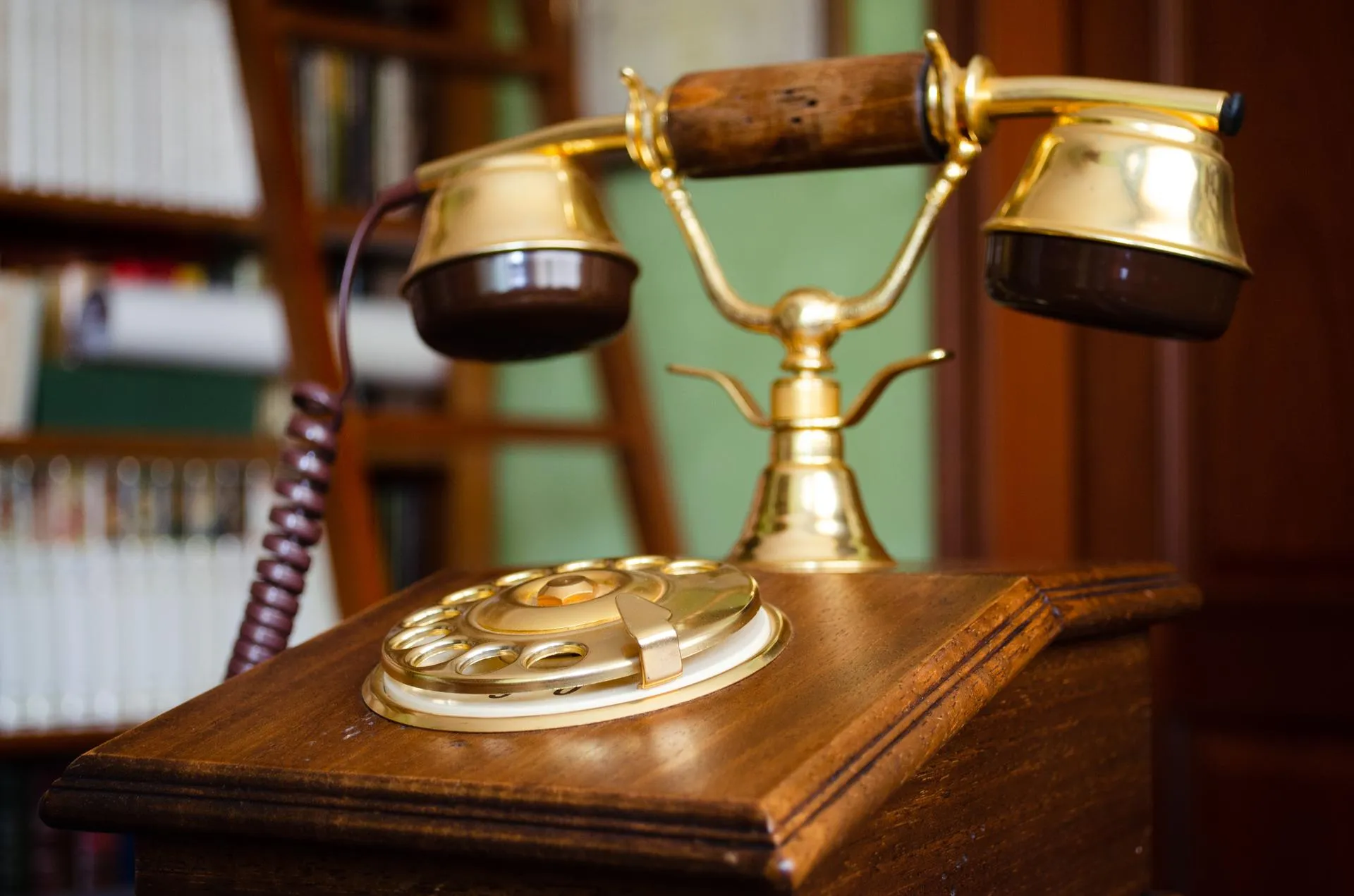 An old wooden telephone with a brass handset in front of bookshelves